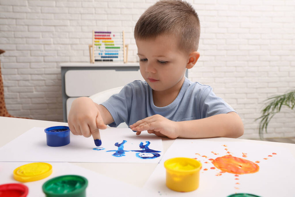 Little boy painting with finger at white table in room - Foto, immagini