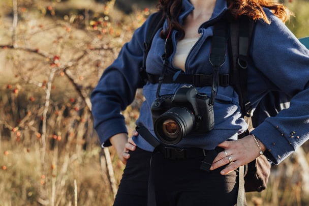 Primo piano di donna da viaggio irriconoscibile con zaino e fotocamera digitale su una cinghia in piedi sul percorso durante la sua escursione - Foto, immagini