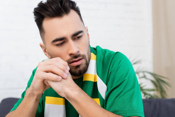 upset sports fan in striped scarf sitting with clenched hands - Фото, изображение