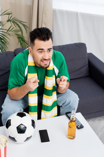 tense man holding crossed fingers for luck near soccer ball, beer and tv remote controller - Φωτογραφία, εικόνα