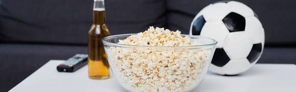 bowl of popcorn near bottle of beer, tv remote controller and soccer ball on table, banner - Photo, Image