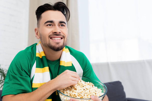veselý sportovní fanoušek s mísou popcornu sledování hry doma - Fotografie, Obrázek