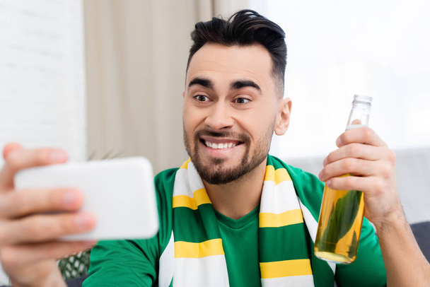 excited sports fan with bottle of beer taking selfie on blurred smartphone - Foto, Bild