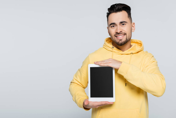 happy man in yellow hoodie holding digital tablet with blank screen isolated on grey - Fotó, kép