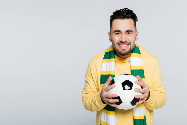 cheerful man in striped scarf holding soccer ball and looking at camera isolated on grey - Photo, image