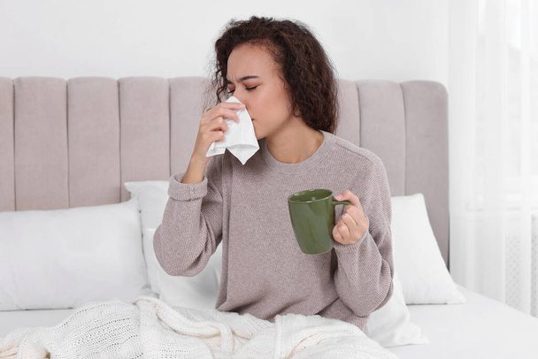 Sick African American woman with tissue and cup of drink in bed at home - Foto, Bild