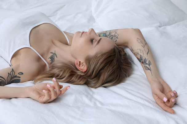Beautiful woman with tattoos on body in bedroom - Фото, изображение
