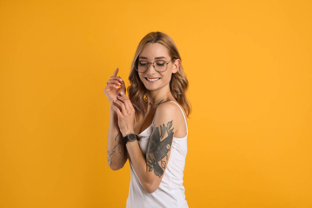Beautiful woman with tattoos on body against yellow background - Foto, imagen