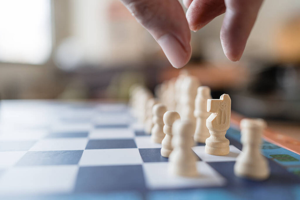 Κλείστε λευκό κομμάτι σκάκι ιππότη στέκεται στη σκακιέρα ανάμεσα σε πιόνια και τα άλλα στη σκακιέρα. Παιχνίδι για πρόκληση και στρατηγικό ανταγωνισμό. - Φωτογραφία, εικόνα