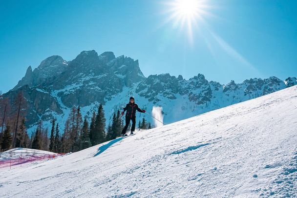 Ο ήλιος λάμπει πάνω από σκιέρ σκι σε χιόνι καλύπτονται τοπίο. Άνδρας τουρίστας απολαμβάνοντας χειμερινό άθλημα σε Άλπεις. Όμορφη μαγευτική οροσειρά ενάντια στον γαλάζιο ουρανό. - Φωτογραφία, εικόνα
