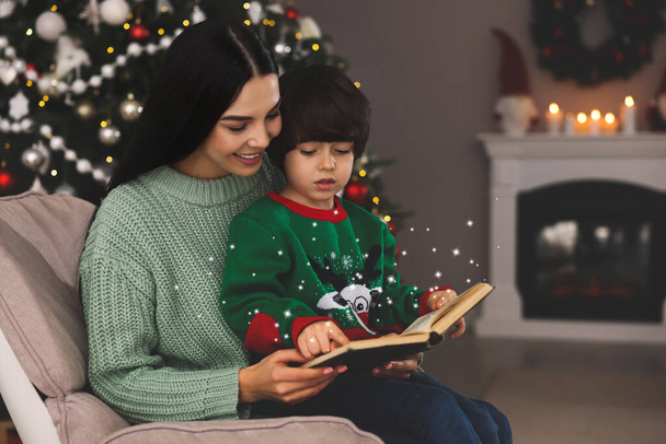 Mother with her cute son reading book in room decorated for Christmas - Fotó, kép