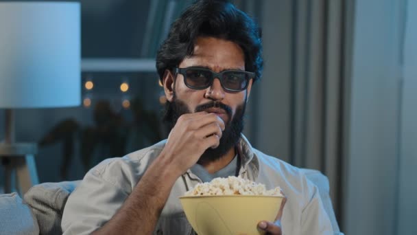 Portrait arabique hispanique latino-indien homme barbu musulman en lunettes 3D regarder la télévision gars détendu dans des lunettes virtuelles profiter d'un programme de film en ligne manger du pop-corn croquant à la maison dans la nuit du soir sombre - Séquence, vidéo