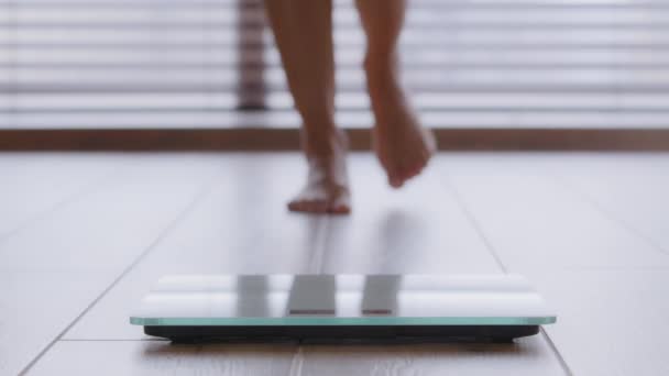 Close-up slanke vrouwelijke benen onherkenbare vrouw lopen blootsvoets door de kamer stappen op elektronische weegschalen controleren gewicht na vetverbranding training thuis lichaamscontrole gewichtsverlies dieet levensstijl - Video