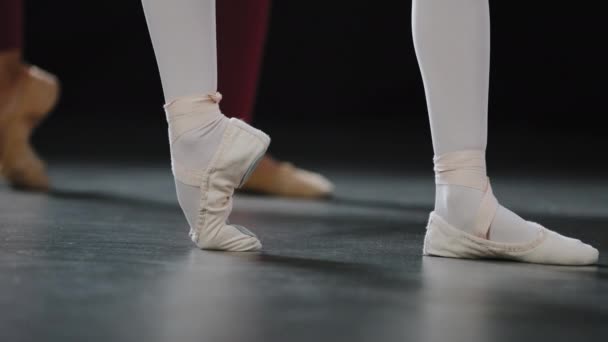 Δύο ζευγάρια γυναικεία πόδια στο πάτωμα στο στάδιο της παράστασης στο στούντιο της τάξης χορού κάνουν ασκήσεις μπαλέτου τεντώνοντας τα πόδια στέκονται στο pointe παπούτσια μπαλαρίνες κορίτσι χορού επαναλαμβάνει τις κινήσεις του εκπαιδευτή δάσκαλος - Πλάνα, βίντεο