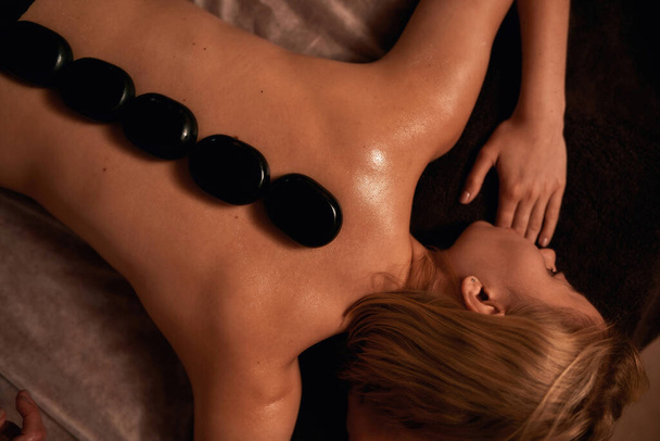 Top view of relaxing woman with hot stones on back - Foto, imagen