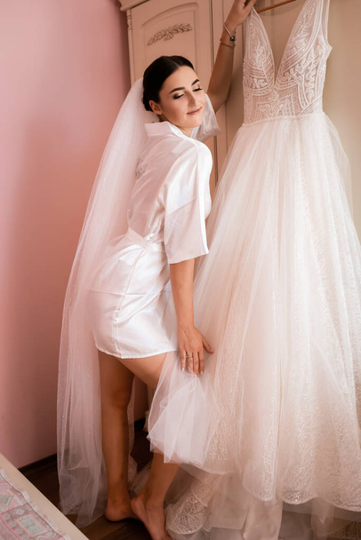 Seksowna panna młoda w buduarze pozująca z suknią ślubną. Szczęśliwa młoda dziewczyna w różowym pokoju. - Zdjęcie, obraz