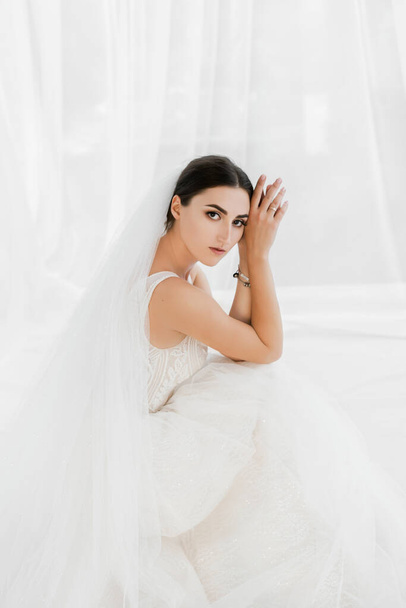 Happy bride with a beautiful long veil and a wedding bouquet. White curtains - Fotó, kép