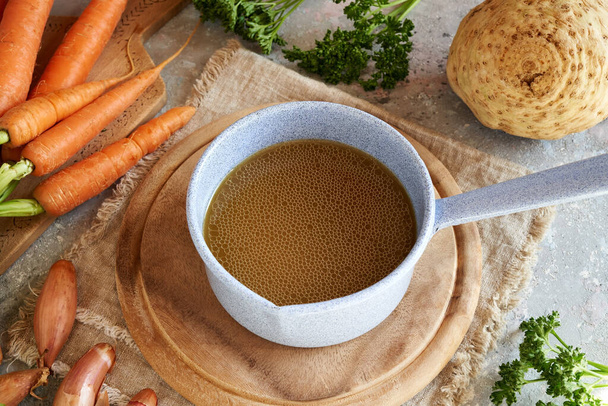 Bone broth in a saucepan with fresh vegetables in the background - Foto, afbeelding
