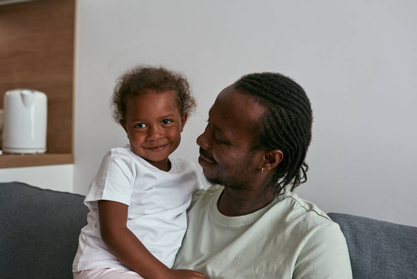 Father hugging joyful daughter on sofa at home - Foto, Imagen