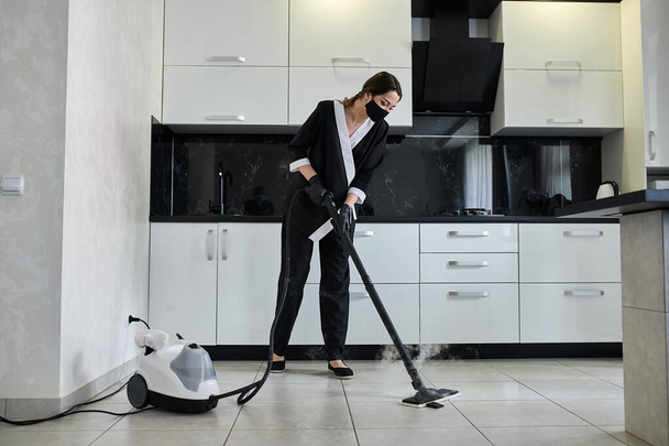 Funcionário da empresa de serviços de limpeza removendo sujeira do chão na cozinha com equipamentos profissionais de limpeza a vapor - Foto, Imagem