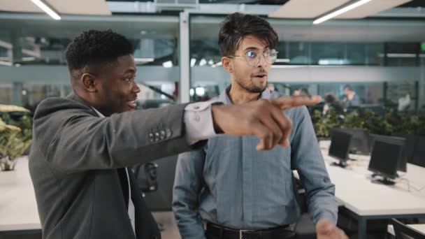 Two co-workers African man boss entrepreneur investor showing Arabian colleague businessman new office place in modern lobby presenting corporate update cheerful friend pointing index finger surprise - Video, Çekim