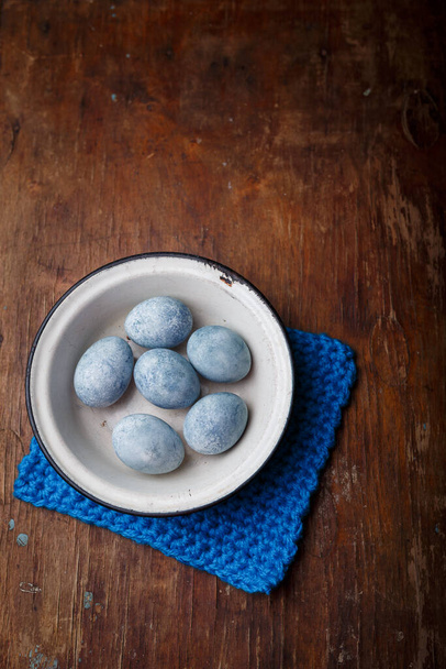 Easter eggs painted blue in white bowl on brown wooden background. Vertical shot, top view on countryside table. - Fotó, kép