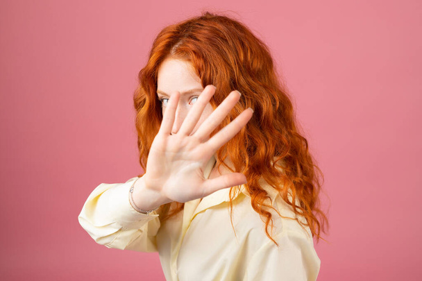 Redhead beautidul woman covering her face with a palm while posing for the camera standing on pink background. - Fotografie, Obrázek