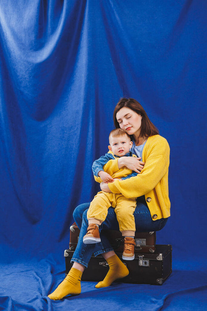 Une jeune mère s'assoit avec un fils de 3 ans dans ses bras, des relations familiales avec un enfant. L'éducation des enfants. Maman avec fils sur un fond bleu - Photo, image
