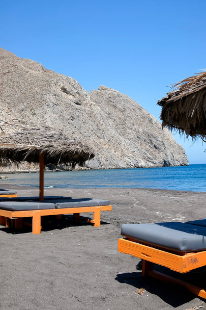 Leere Liegestühle und Sonnenschirme am berühmten Sandstrand von Perissa auf Santorin - Foto, Bild