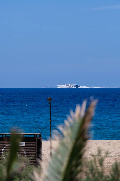 Ios, Grécia - 16 de maio de 2021: Um barco de balsa passando em frente à famosa praia de Mylopotas, em Ios Grécia - Foto, Imagem