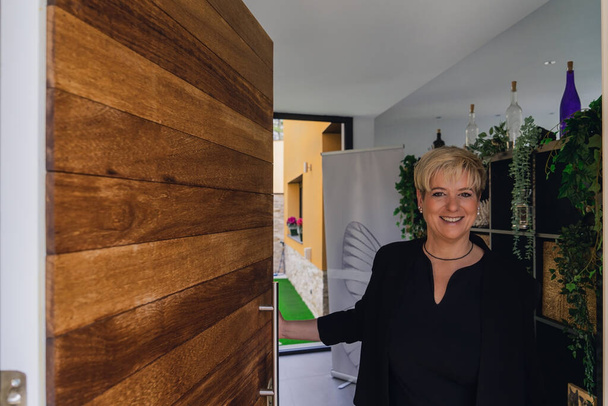 Adult businesswoman greeting a customer in her small spa business. Business owner opening the door to greet the client. - Fotoğraf, Görsel