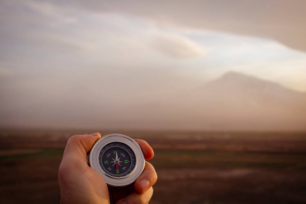 mit einem Kompass vor dem Hintergrund eines Berges bei Sonnenuntergang - Foto, Bild