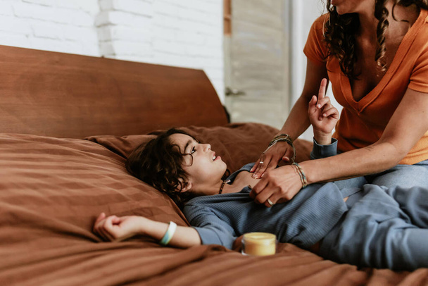 Hispanische Mutter legt Creme, Salbe oder Balsam für ihren Sohn zu Hause in Mexiko Lateinamerika auf das Bett - Foto, Bild