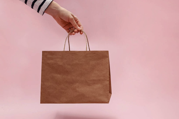 Woman's hand holding paper bag over the pink background. Mock-up with place for text - Foto, Imagen
