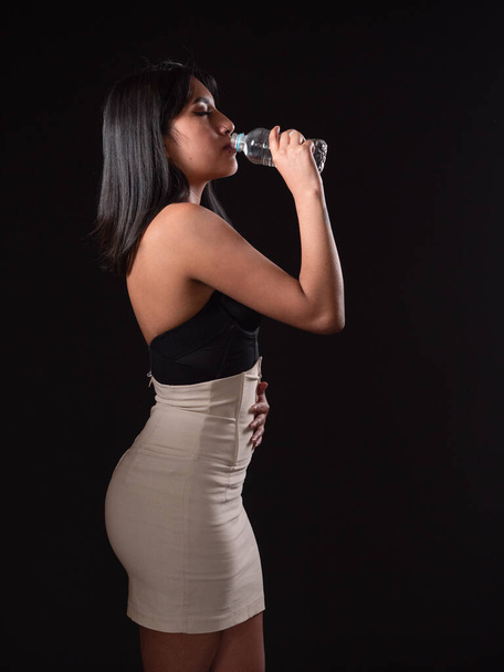 mujer hispana sosteniendo un vaso de agua aislado sobre fondo negro - Foto, imagen