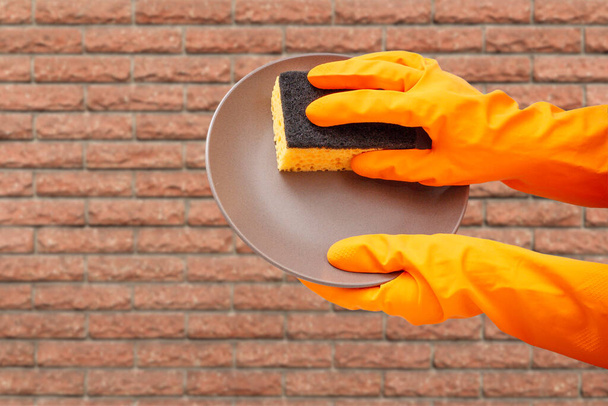 Frauenhände in orangefarbenen Schutzhandschuhen mit Teller und Schwamm. Wasch- und Reinigungskonzept. - Foto, Bild