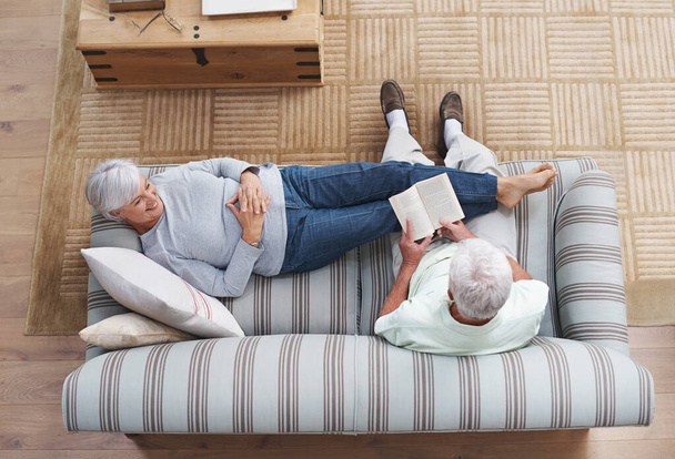La poésie est le langage de l'amour.... Un homme âgé lisant à sa femme alors qu'elle est allongée sur le canapé. - Photo, image