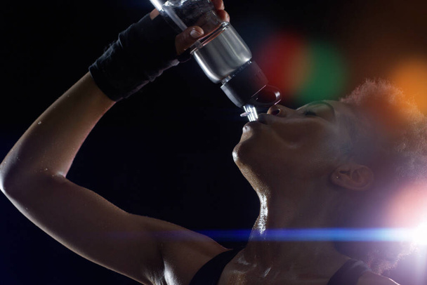 Nada sabe mejor que esto después de un entrenamiento intenso. Estudio de una joven deportista bebiendo de una botella de agua sobre un fondo oscuro. - Foto, Imagen