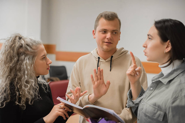 Two girls and a guy are talking in sign language. Three deaf students chatting in a university classroom. - Foto, Imagen
