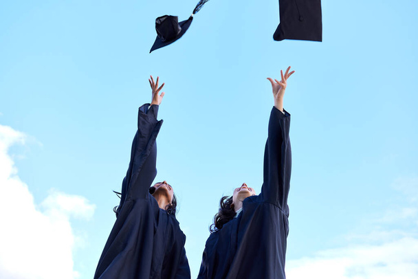 The famous graduation day tradition. Low angle shot of two attractive young female students celebrating on graduation day. - Foto, Imagen