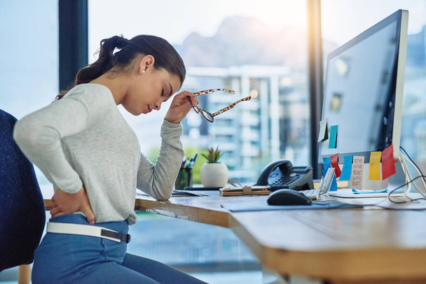 Der Versuch, durch die Schmerzen eines schweren Tages zu kommen. Aufnahme einer jungen Geschäftsfrau, die unter Rückenschmerzen leidet, während sie im Büro arbeitet. - Foto, Bild