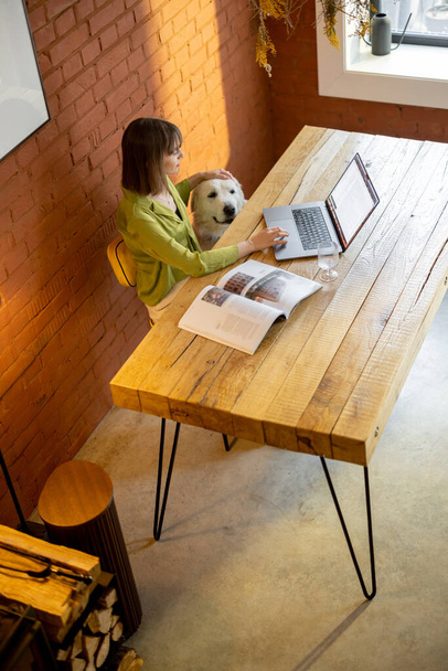 Žena pracuje na notebooku, zatímco sedí u dřevěného stolu v útulném obývacím pokoji - Fotografie, Obrázek