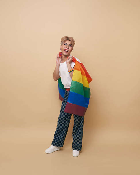 Gioventù asiatica transgender LGBT con bandiera arcobaleno sulla spalla isolata su sfondo di colore nudo. Uomo con un gay orgoglio bandiera concetto. - Foto, immagini