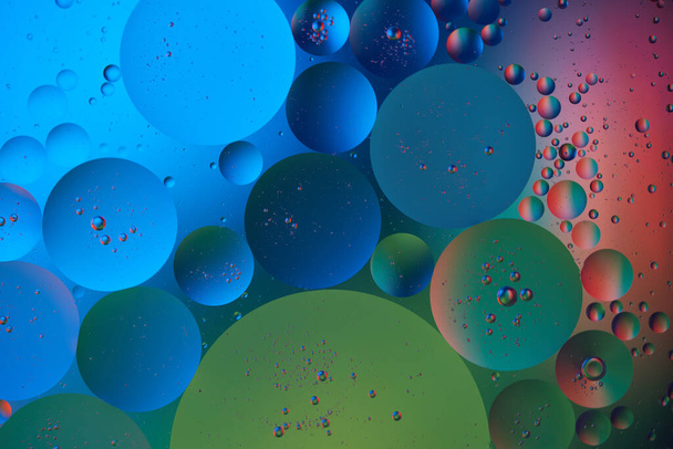Fond coloré abstrait, bulles violettes et cercles dans l'eau huileuse. Couleurs bleu, rouge et vert. Photographie macro. Vue du dessus. - Photo, image