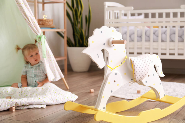 Classic rocking horse and adorable baby girl in playroom - Photo, image
