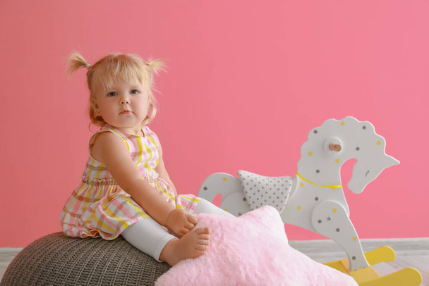 Suloinen vauva tyttö tyyny istuu pouf lähellä keinuhevonen - Valokuva, kuva