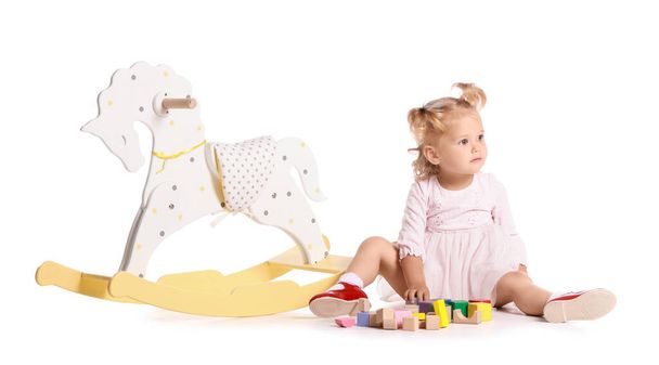Entzückendes Baby-Mädchen mit Schaukelpferd und Spielzeug auf weißem Hintergrund - Foto, Bild