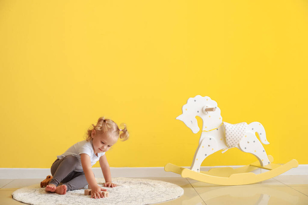 Suloinen vauva tyttö keinuvat hevonen ja lelut lähellä keltaista seinää - Valokuva, kuva