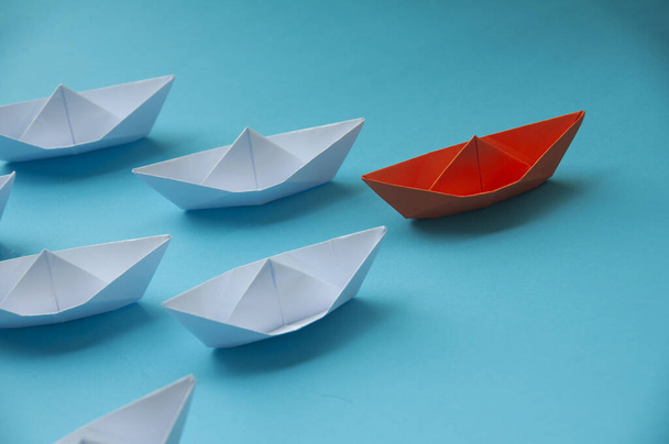 Concepto de liderazgo - Origami de barco de papel de color naranja que lidera el resto de la nave de papel blanco sobre fondo de cubierta azul. Copiar espacio - Foto, imagen