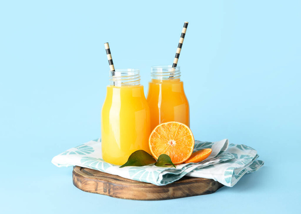 Bouteilles de jus de mandarine frais sur fond bleu - Photo, image